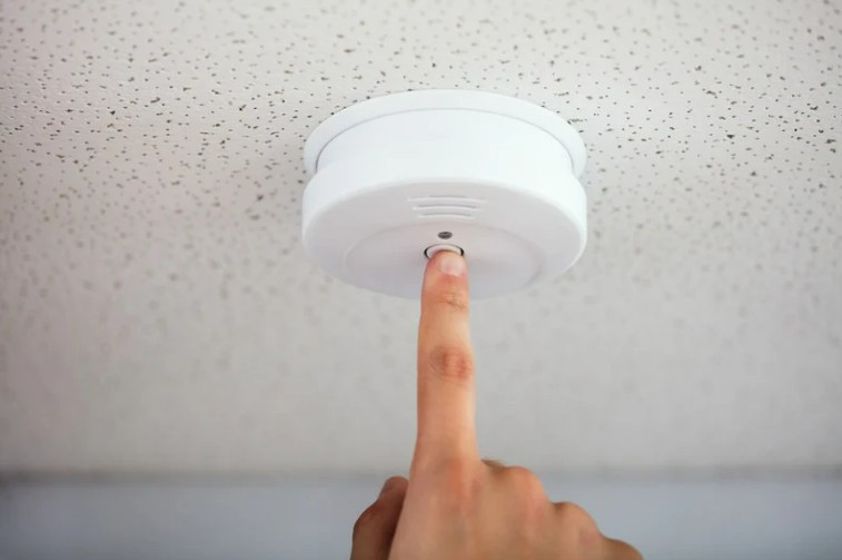 Close up of finger pressing button on beeping smoke alarm